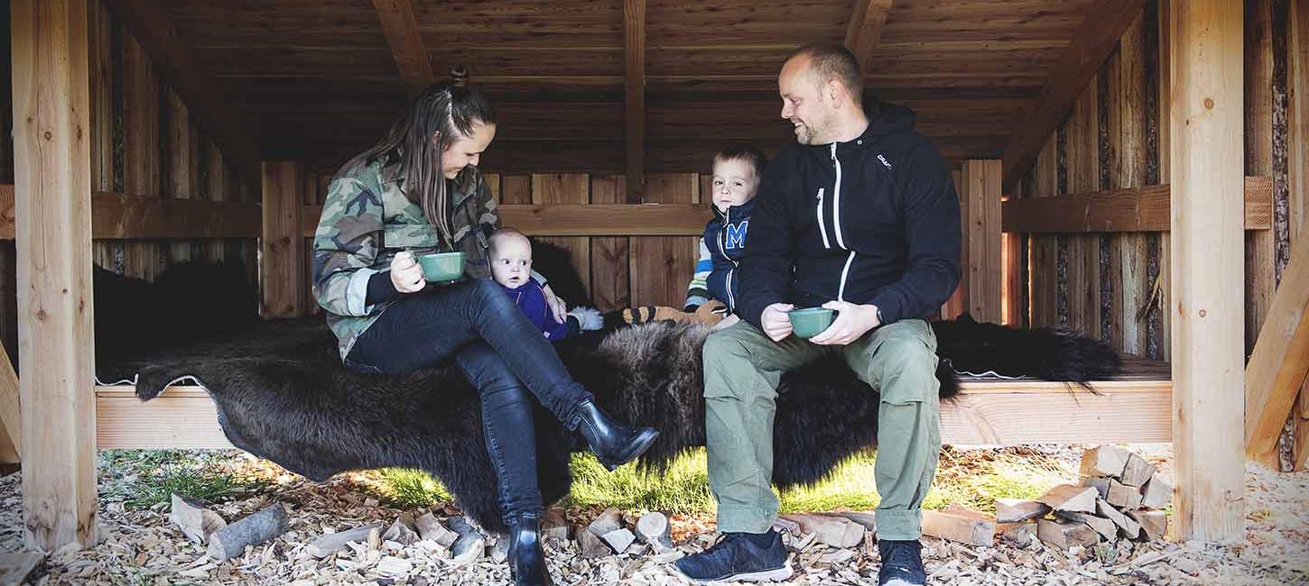 Mutter, Vater und zwei kleine Kinder entspannen sich auf einem Bisonversteck in einem großen Unterstand