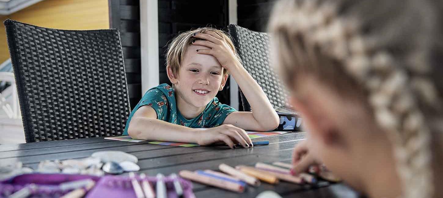 Dreng smiler til sin søster ved bordet i sommerhuset