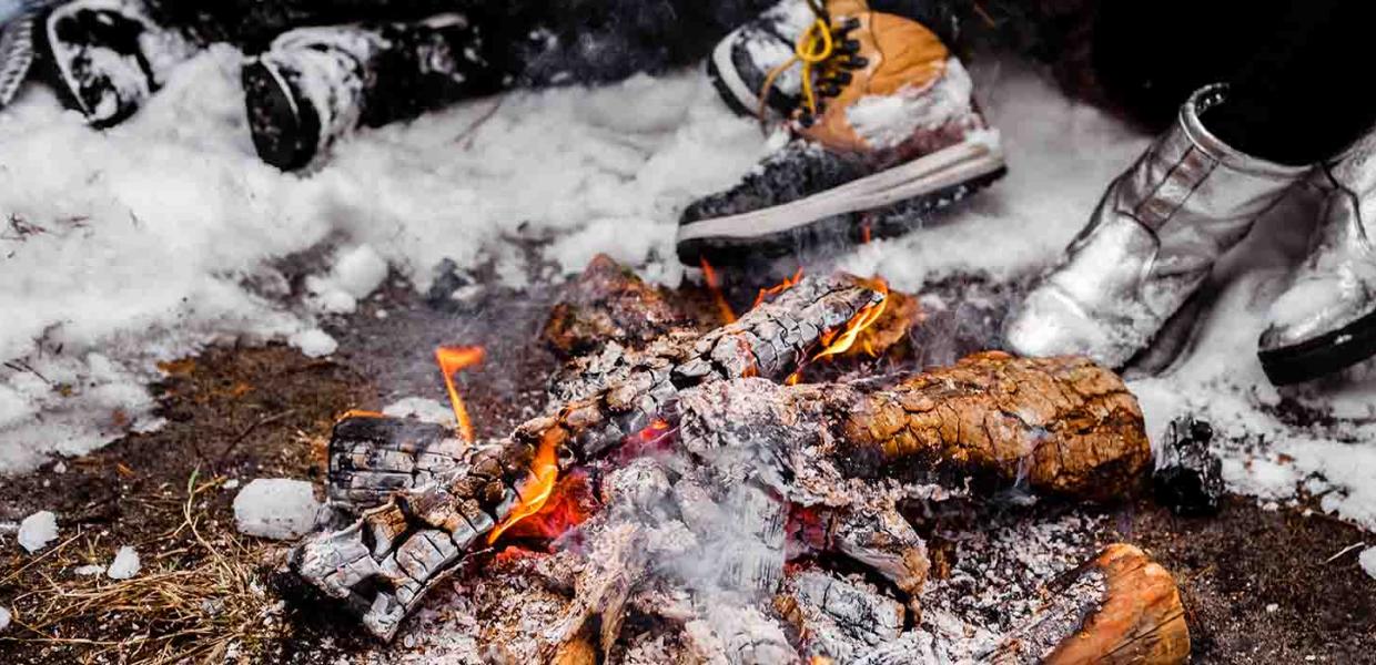 Menschen sitzen in einem verschneiten Winter mit großen Stiefeln am brennenden Feuer
