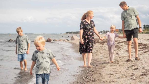 Familie med tre børn går tur på stranden